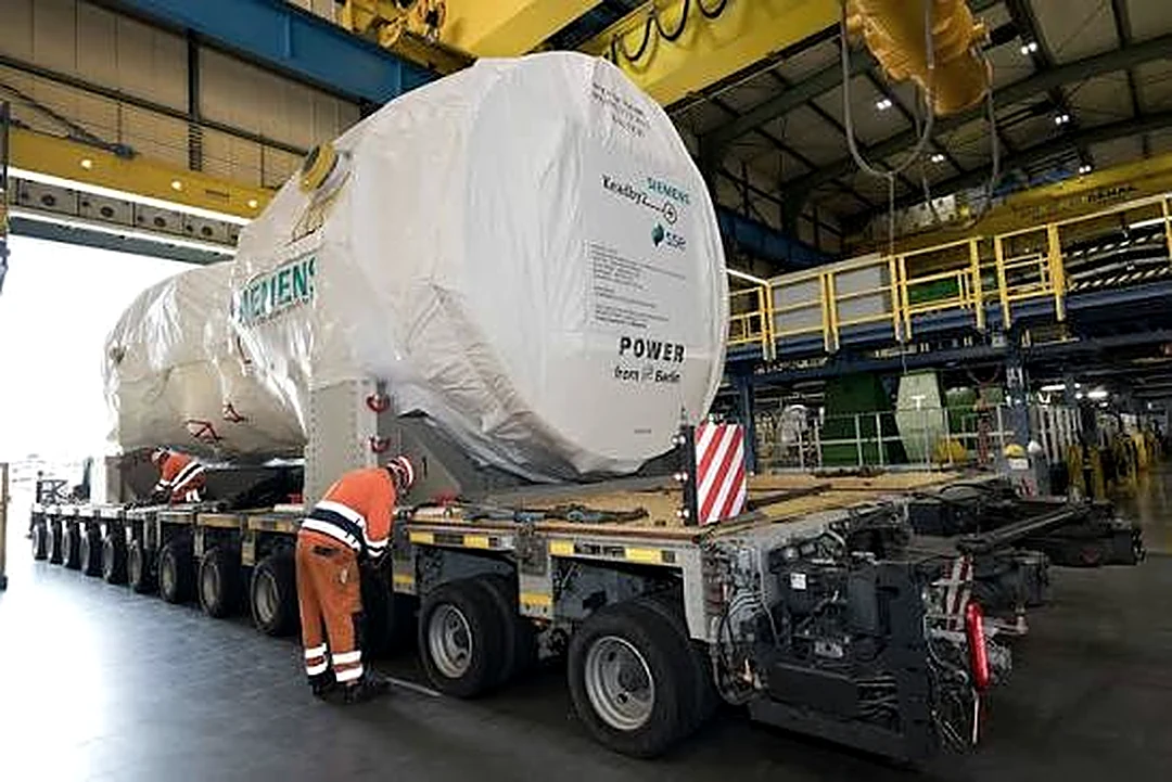 Wrapped gas turbine package loaded on a multi-axle heavy-haul trailer with a rigger alongside